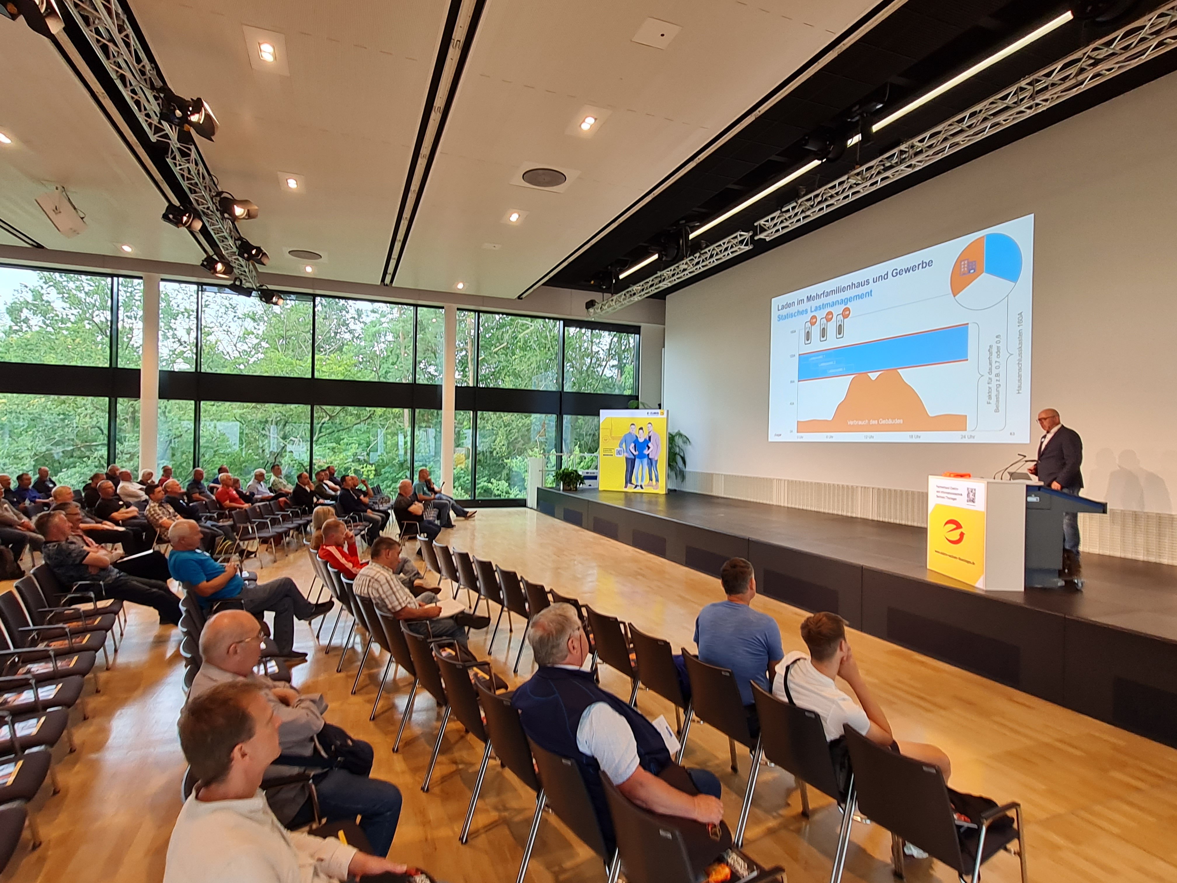 Bild mit seitlichen Blick in den Veranstaltungsraum der Fachschulungstage 2024 in Dresden. Auf der Tribüne steht ein Referent der seinen Vortrag hält, in den Tischreihen davor sitzen die Teilnehmer.