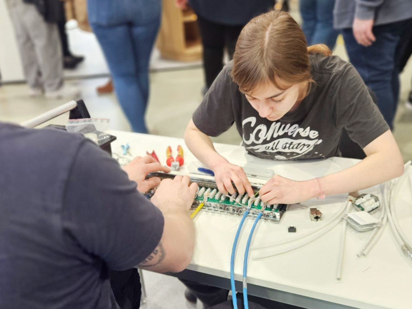 Eine Besucherin des Messestandes sitz an einem Tisch und versucht sich an einer elektrischen Schaltanlage mit mehreren Kabeln.