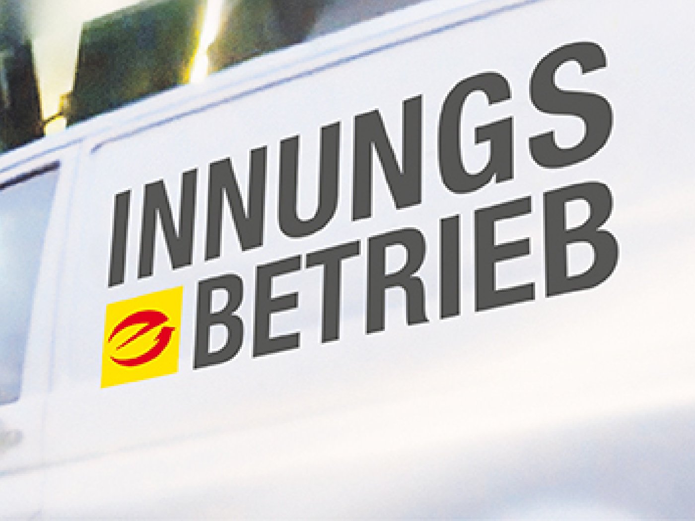 Foto zeigt einen weißen Transporter, auf diesem ist seitlich eine Fahrzeugbeklebung aufgebracht mit der Aufschrift "Innungsbetrieb". Neben der Aufschrift ist das E-Marken-Logo positioniert.