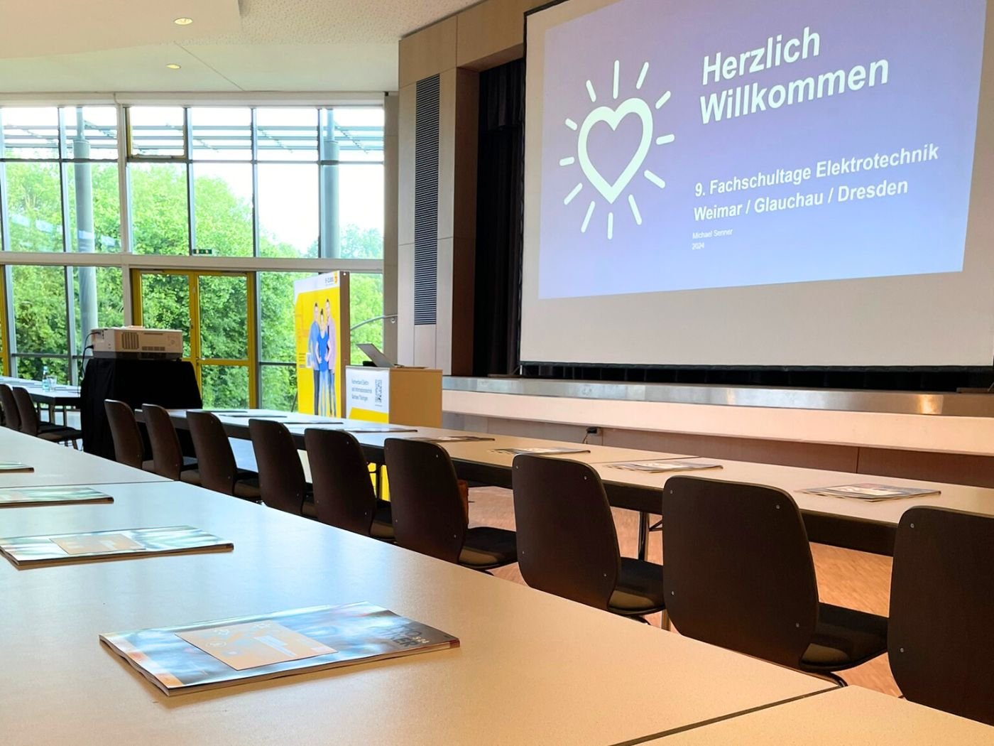 Bild mit seitlichen Blick in den Veranstaltungsraum der Fachschulungstage 2024 in Glauchau. Auf der Tribüne ist eine Folie einer Powerpoint-Präsentation auf der Leinwand abgebildet.