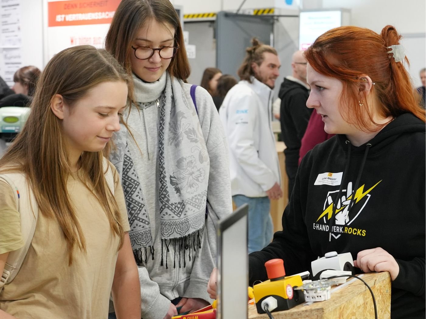 Interessierte junge Besucherinnen stehen interessiert am Messestand und sind mit einer Standbetreuerin im Gespräch.