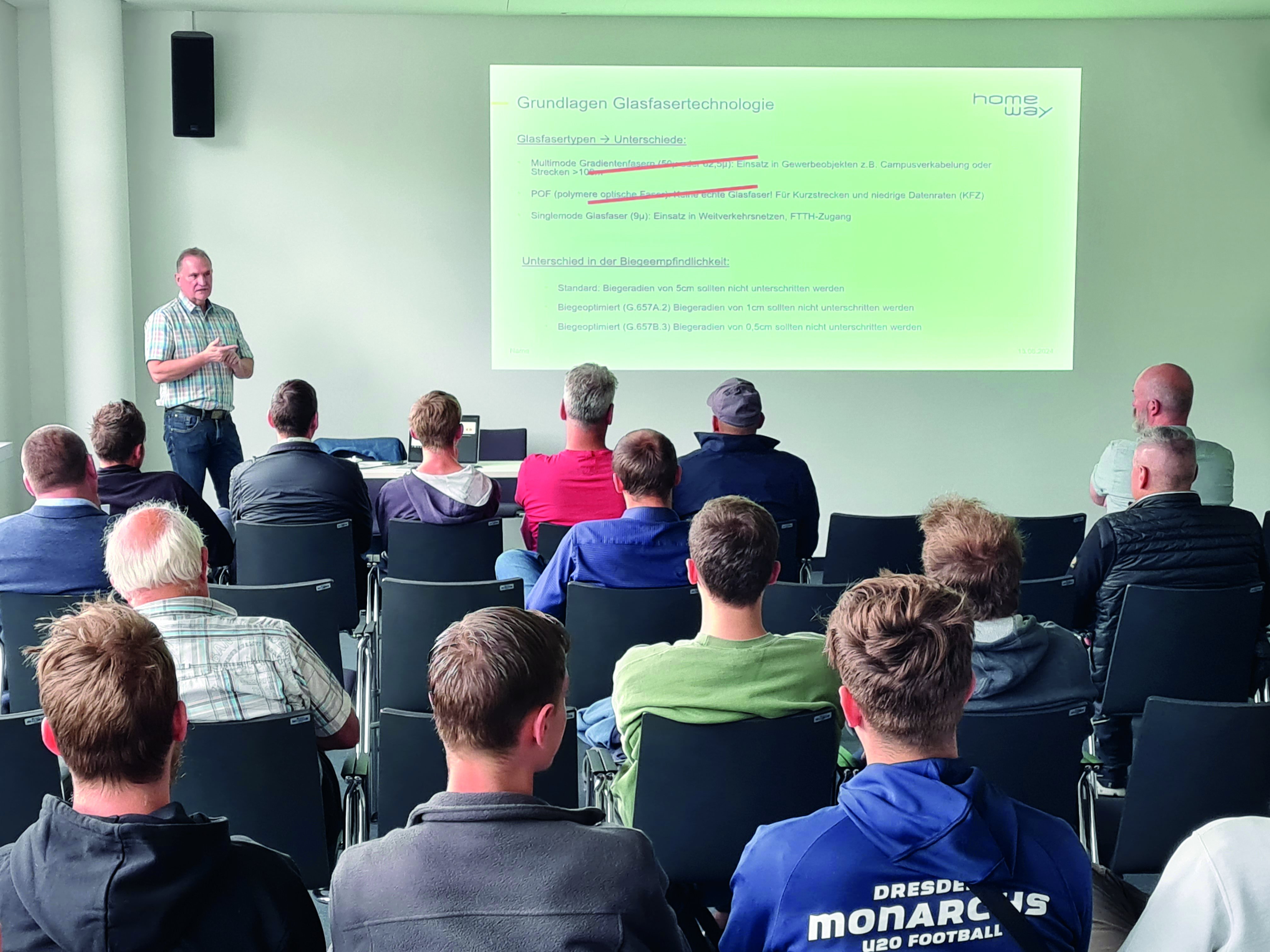 Bild mit Blick in den Veranstaltungsraum der Fachschulungstage 2024 in Dresden. Auf der Tribüne steht ein Referent der seinen Vortrag hält, in den Tischreihen davor sitzen die Teilnehmer.